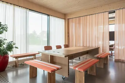 Møterom med Høvel sittebenker, langbord, betonggulv, ribbet trehimling, oransje gardiner.